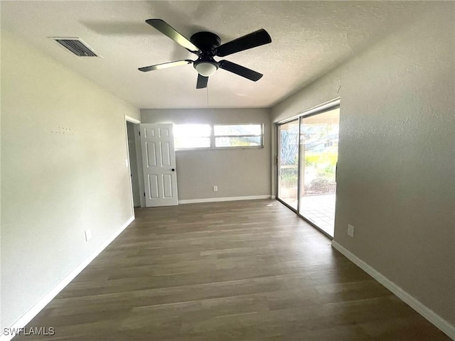 empty room featuring dark wood-style floors, a textured ceiling, visible vents, and baseboards