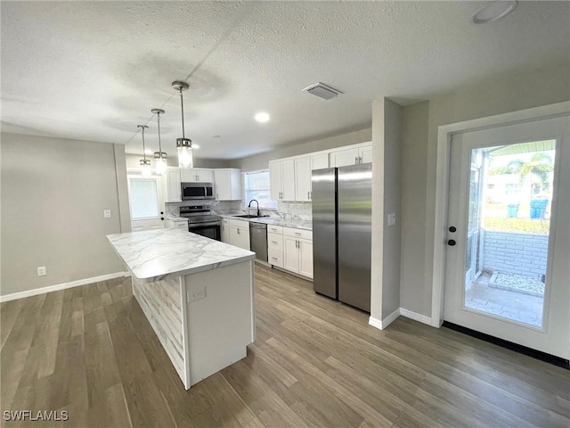 kitchen featuring stainless steel appliances, a kitchen island, pendant lighting, white cabinets, and sink