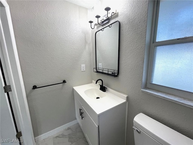 half bath with marble finish floor, a textured wall, toilet, vanity, and baseboards