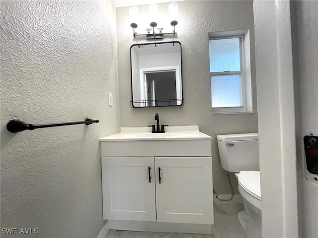 half bathroom featuring toilet, a textured wall, baseboards, and vanity