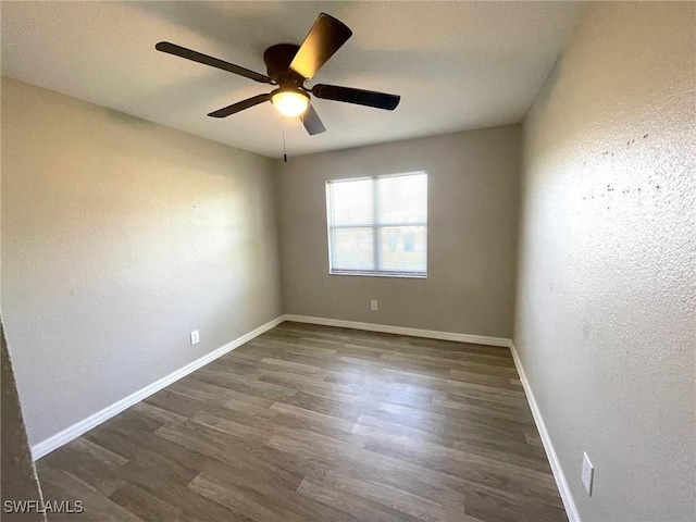 spare room featuring ceiling fan, baseboards, and dark wood-type flooring