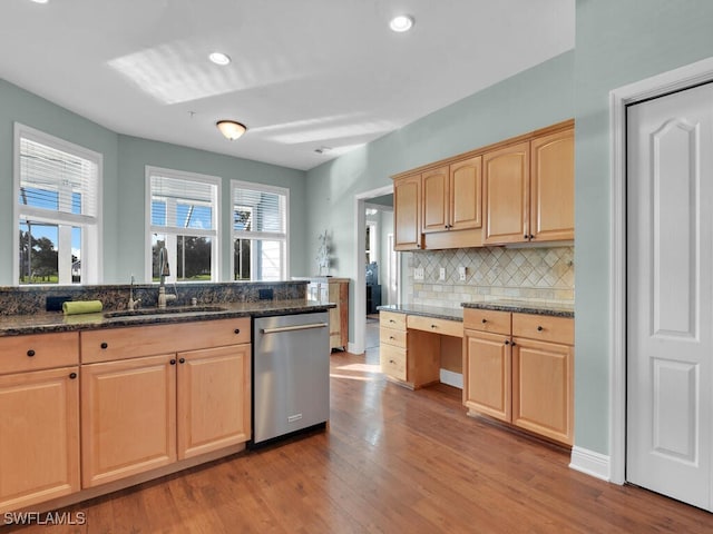 kitchen with sink, stainless steel dishwasher, dark stone countertops, light brown cabinetry, and light hardwood / wood-style floors