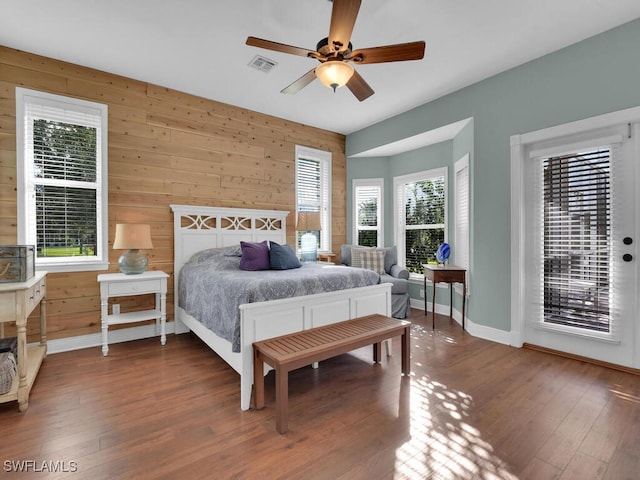 bedroom with access to exterior, wood walls, ceiling fan, and dark hardwood / wood-style floors