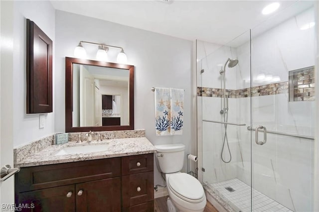 bathroom featuring hardwood / wood-style flooring, a shower with door, vanity, and toilet