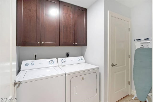 washroom with cabinets, washing machine and dryer, and light hardwood / wood-style flooring