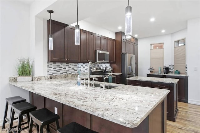 kitchen with tasteful backsplash, appliances with stainless steel finishes, decorative light fixtures, light hardwood / wood-style floors, and kitchen peninsula