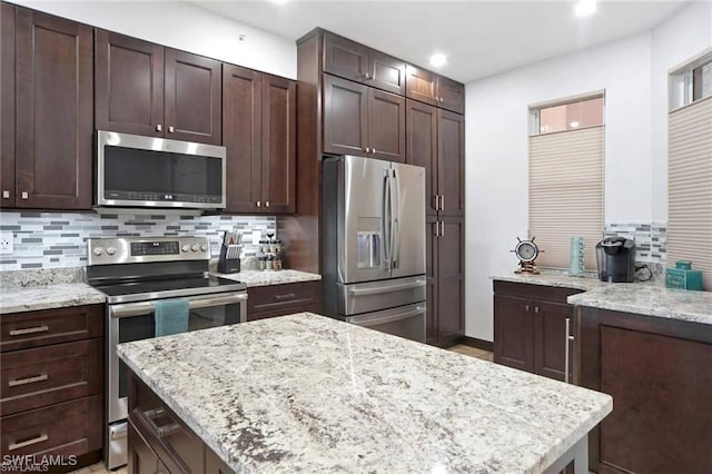 kitchen featuring dark brown cabinets, decorative backsplash, appliances with stainless steel finishes, and light stone counters