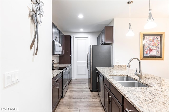 kitchen with light stone counters, stainless steel appliances, hanging light fixtures, sink, and light hardwood / wood-style flooring