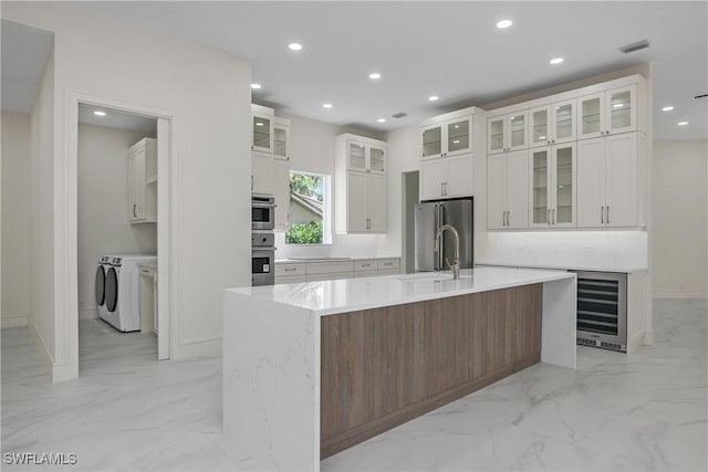 kitchen featuring a kitchen island with sink, sink, separate washer and dryer, white cabinetry, and wine cooler