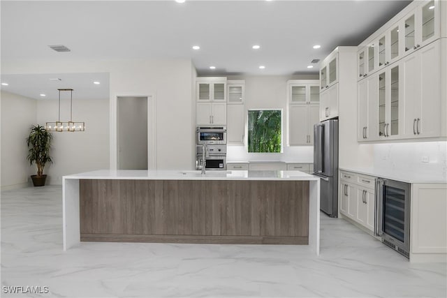 kitchen featuring white cabinets, appliances with stainless steel finishes, a center island with sink, and beverage cooler