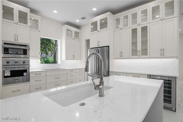 kitchen featuring light stone countertops, appliances with stainless steel finishes, sink, white cabinetry, and wine cooler