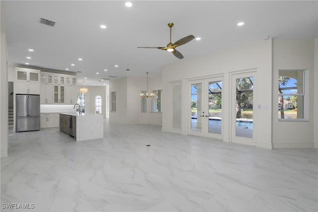 unfurnished living room featuring french doors, sink, and ceiling fan with notable chandelier