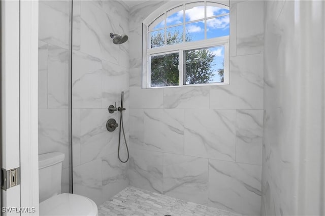 bathroom with a tile shower and toilet