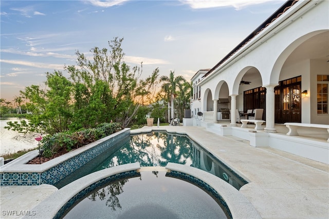 pool at dusk featuring an in ground hot tub and a patio