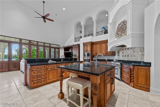 kitchen with a high ceiling, a kitchen breakfast bar, stainless steel appliances, a center island with sink, and sink