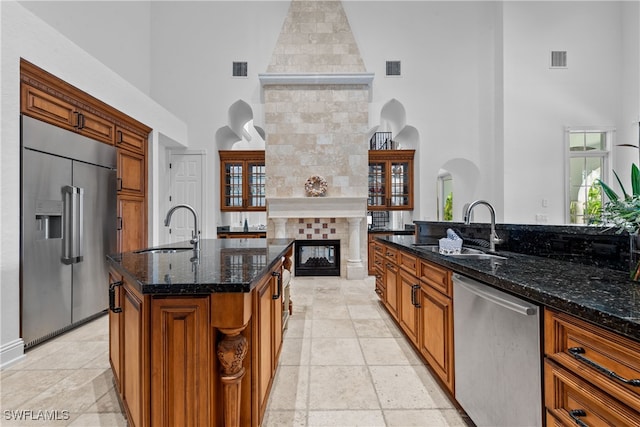 kitchen featuring a kitchen island with sink, sink, appliances with stainless steel finishes, a fireplace, and a towering ceiling