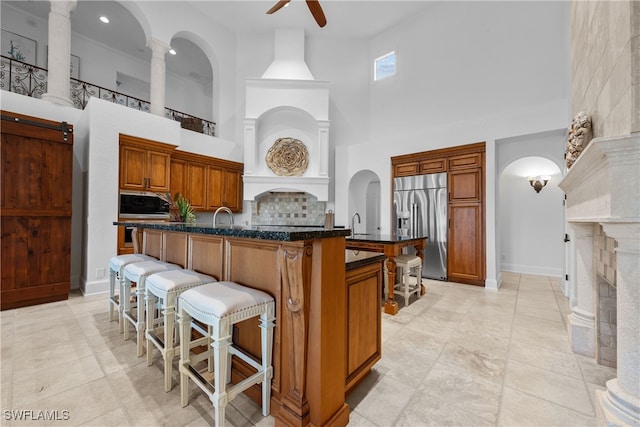 kitchen featuring light tile patterned flooring, a kitchen breakfast bar, ceiling fan, a high ceiling, and stainless steel built in fridge