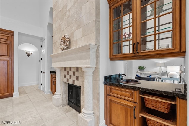 bar featuring a tiled fireplace, dark stone counters, and light tile patterned floors