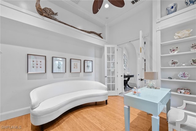 sitting room with ceiling fan, wood-type flooring, built in features, a towering ceiling, and french doors