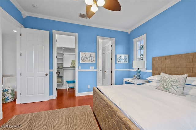 bedroom with a spacious closet, ceiling fan, crown molding, and dark hardwood / wood-style flooring