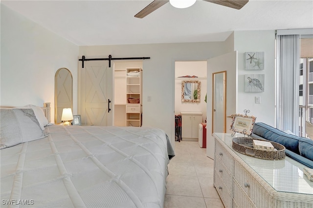 bedroom with a barn door, a spacious closet, a closet, ceiling fan, and light tile patterned floors