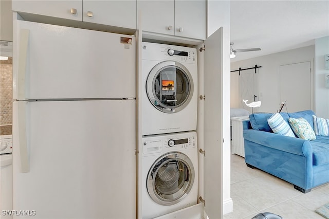 laundry room featuring light tile patterned flooring, stacked washer and clothes dryer, and a barn door