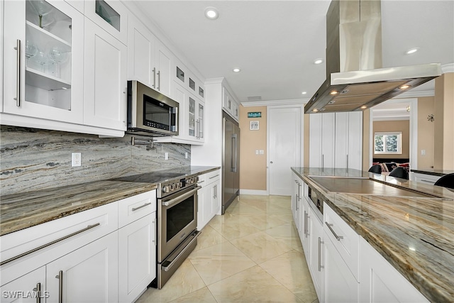 kitchen with island exhaust hood, backsplash, dark stone counters, premium appliances, and white cabinetry