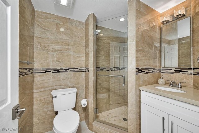 bathroom with a shower with door, vanity, tile walls, and toilet