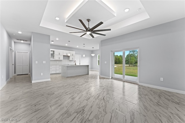 unfurnished living room with ceiling fan, a raised ceiling, and sink