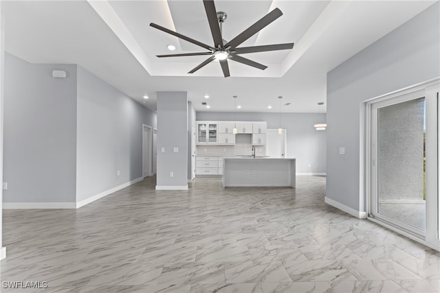 unfurnished living room featuring sink, a tray ceiling, and ceiling fan