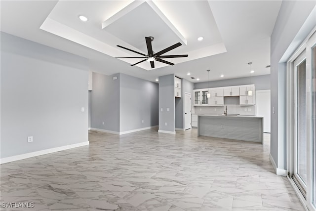 unfurnished living room featuring sink, a raised ceiling, and ceiling fan