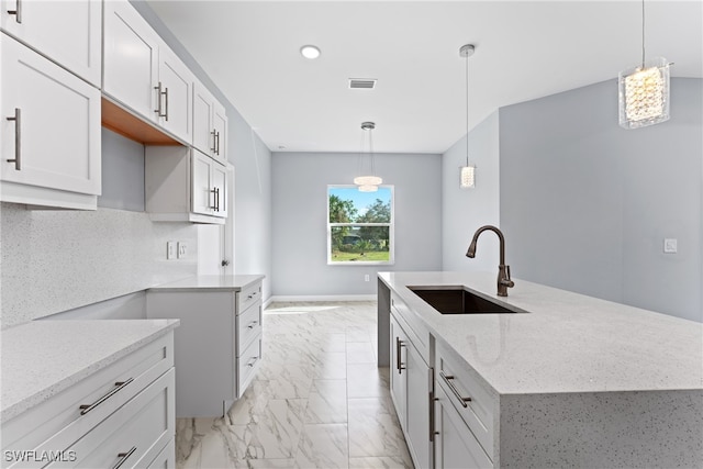 kitchen featuring tasteful backsplash, light stone countertops, sink, white cabinetry, and decorative light fixtures