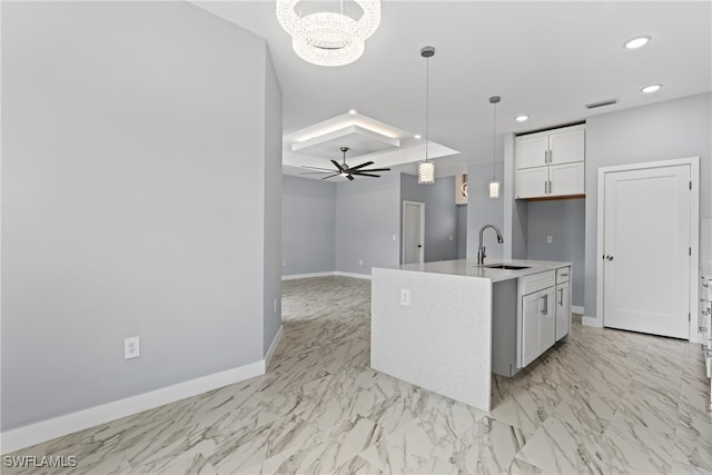 kitchen featuring white cabinets, an island with sink, ceiling fan with notable chandelier, pendant lighting, and sink