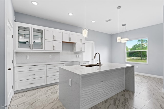 kitchen with sink, an island with sink, decorative light fixtures, and white cabinets