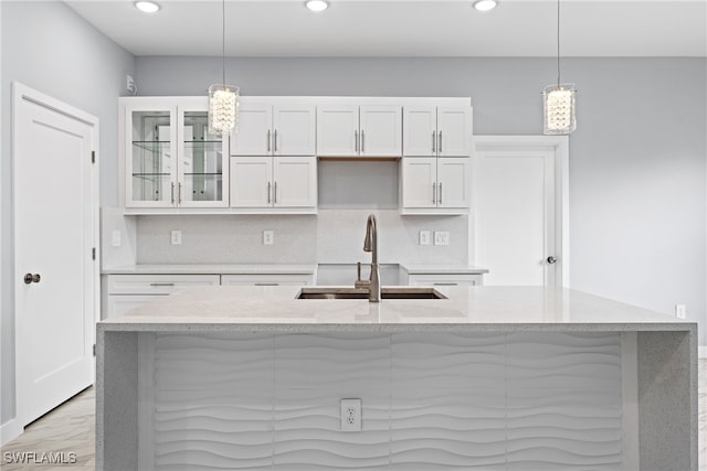 kitchen with sink, pendant lighting, white cabinets, light hardwood / wood-style flooring, and a kitchen island with sink