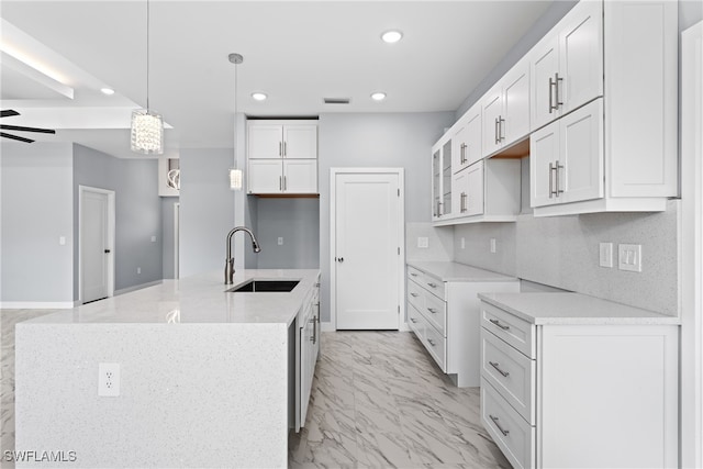 kitchen with sink, white cabinetry, ceiling fan, decorative light fixtures, and a kitchen island with sink