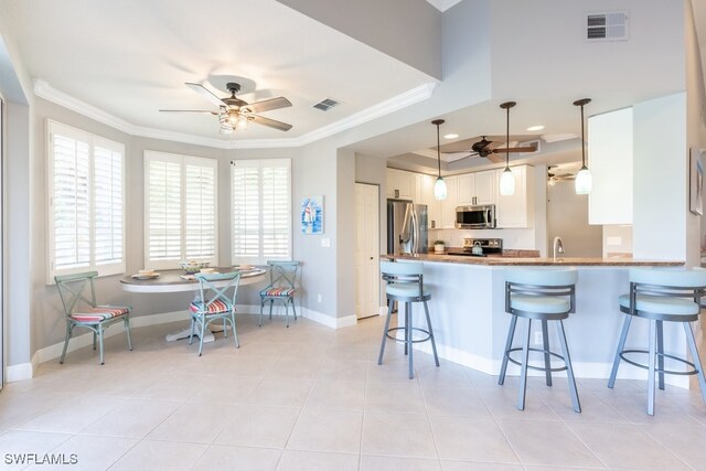 kitchen featuring a kitchen bar, stainless steel appliances, pendant lighting, kitchen peninsula, and white cabinetry