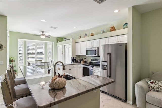 kitchen with sink, a kitchen bar, stainless steel appliances, white cabinets, and light tile patterned floors