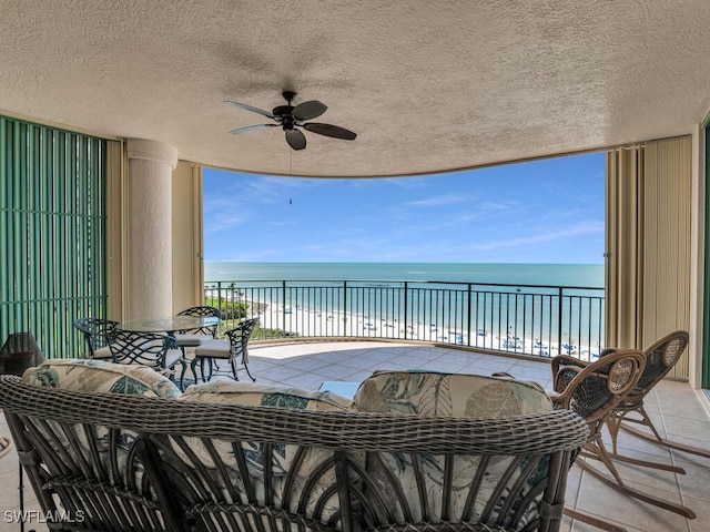 balcony with a patio, a water view, a view of the beach, and ceiling fan