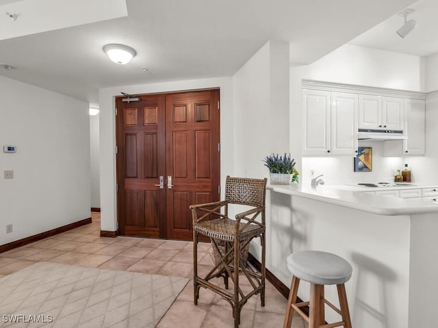 kitchen featuring kitchen peninsula, white cabinets, white stovetop, light tile patterned floors, and a breakfast bar