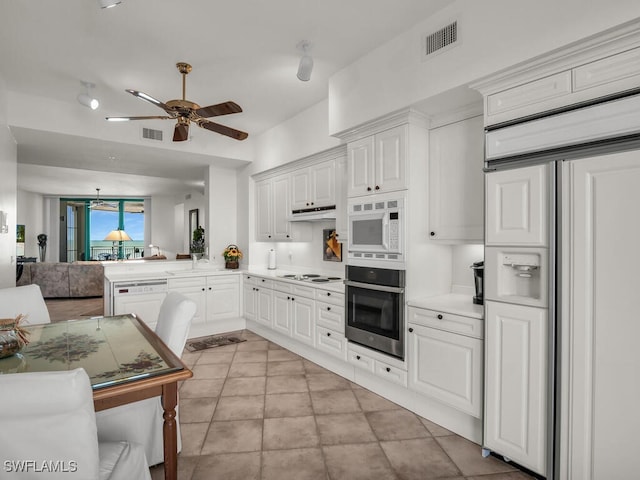 kitchen with built in appliances, kitchen peninsula, light tile patterned floors, white cabinets, and ceiling fan