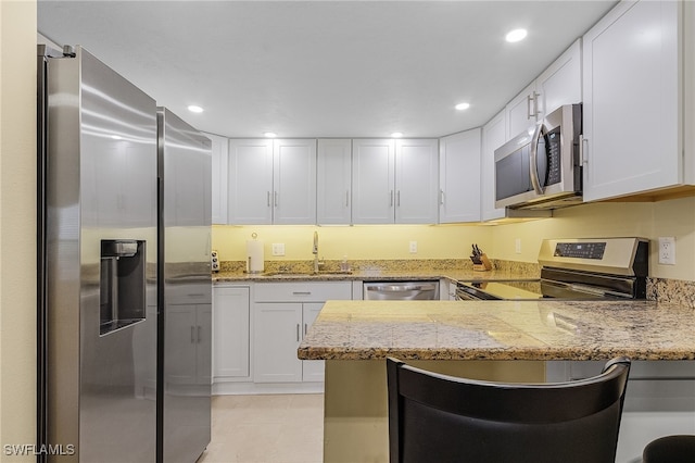 kitchen with kitchen peninsula, stainless steel appliances, sink, white cabinetry, and light stone counters