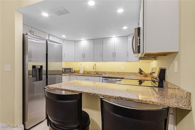 kitchen with kitchen peninsula, white cabinets, a kitchen breakfast bar, light stone countertops, and stainless steel appliances