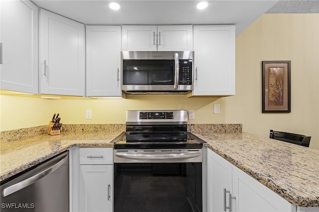 kitchen featuring kitchen peninsula, white cabinets, stainless steel appliances, and light stone counters