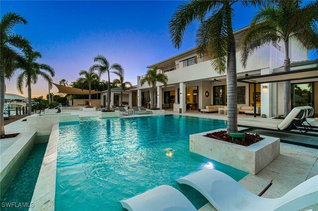 pool at dusk with ceiling fan and a patio area