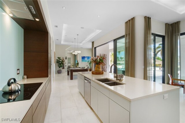 kitchen with sink, a tray ceiling, a kitchen island with sink, black electric stovetop, and white cabinets