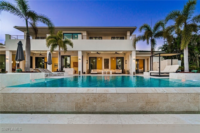 pool at dusk with an outdoor living space, ceiling fan, a patio area, and a hot tub