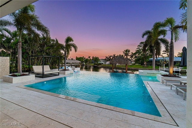 pool at dusk featuring pool water feature, a gazebo, a water view, and a patio