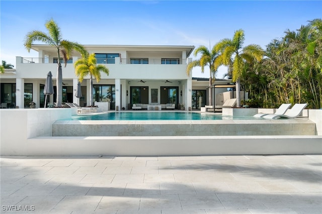 back of property with a swimming pool with hot tub, a balcony, ceiling fan, and a patio