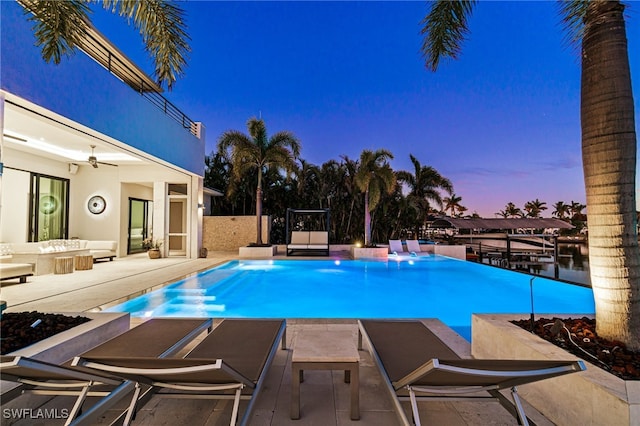 pool at dusk featuring a patio area and ceiling fan